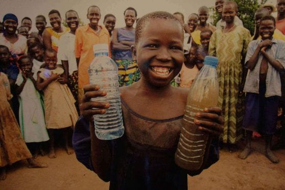 a child holding a bottle of clean water and a bottle of dirty water