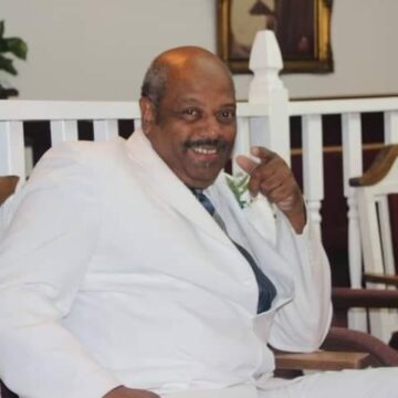 LARRY IN WHITE SUIT SITTING IN PULPIT